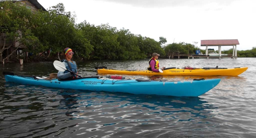 A person in a yellow kayak paddles beside a person in a blue kayak on calm water. 